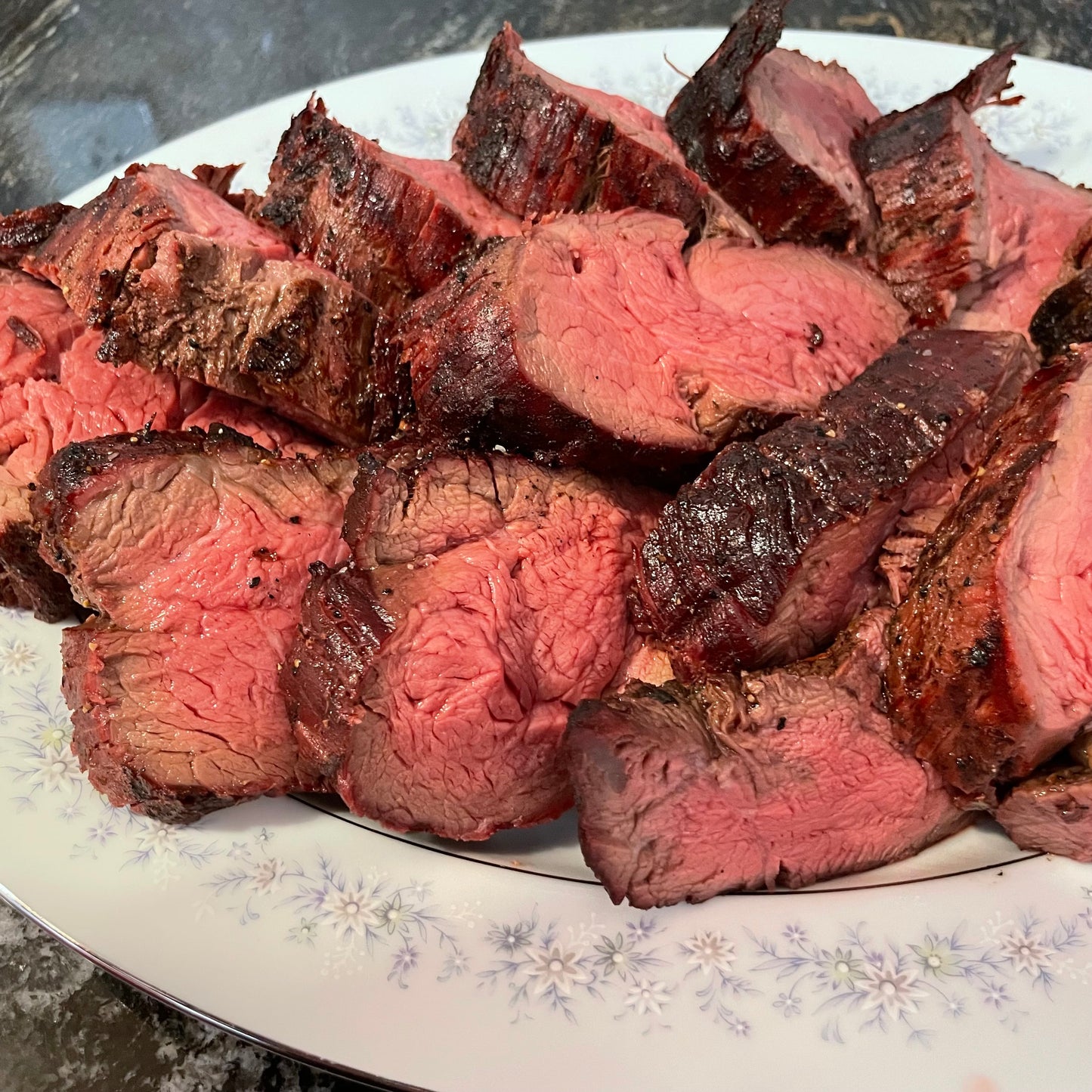 Sliced grass fed beef tenderloin on a decorative plate with a floral pattern